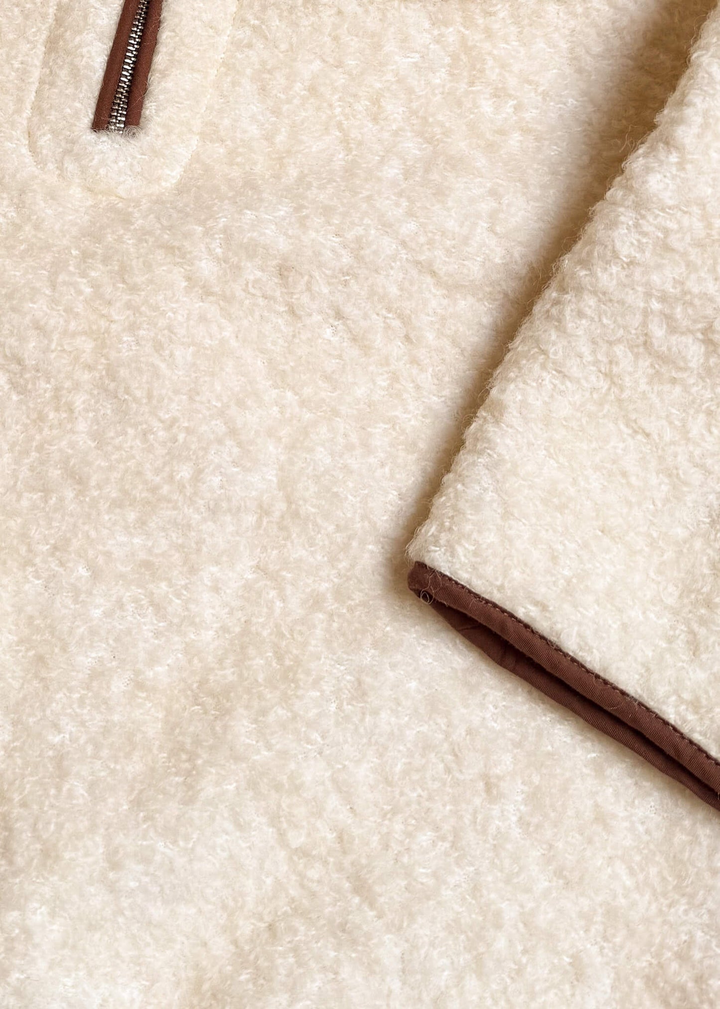 Zbliżenie na strukturę wełny bluzy Teddy ecry i brązową lamówkę.