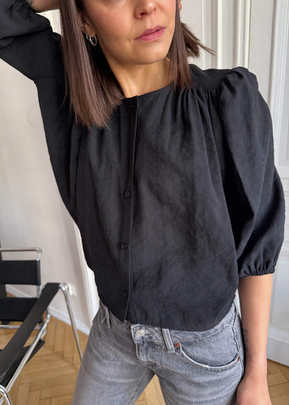 Koszula Nell ASIDE, czarna z żakardowej tkaniny w kwiaty, bufiastym rękawem, zapinana na guziki.