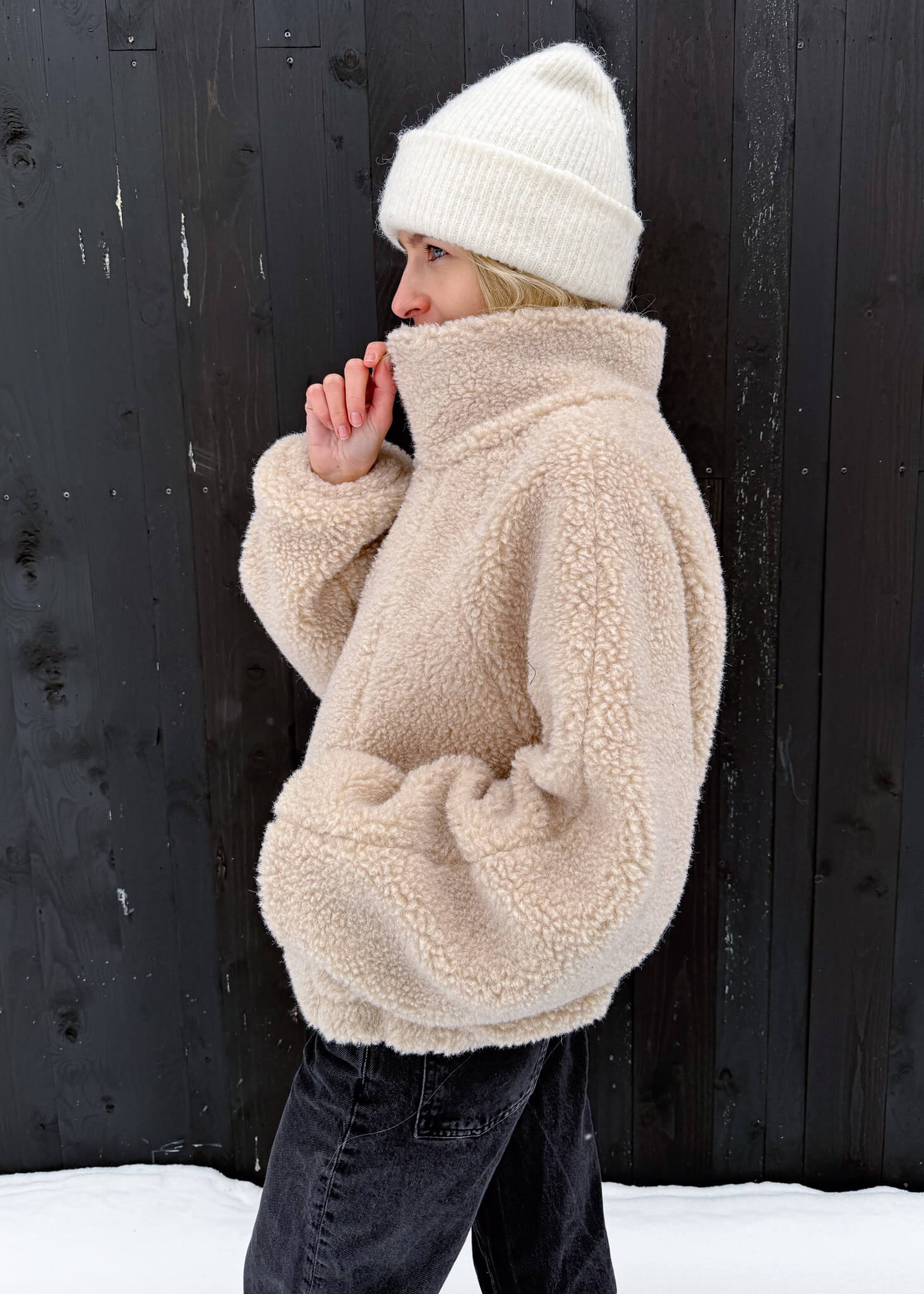 Beżowa kurtka polarowa ASIDE z wełny merino z wysokim kołnierzem, zapinana na zamek.